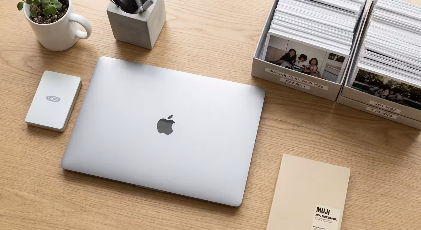 An organized desk with a laptop, hard drive, and neat stacks of photos.