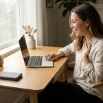 A woman happily organizing photos on her laptop at a bright, minimalist desk.