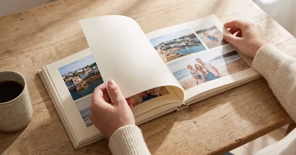 Close-up of hands turning the pages of a high-quality linen photo book on a wooden table in soft light.