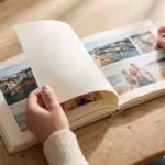 Close-up of hands turning the pages of a high-quality linen photo book on a wooden table in soft light.