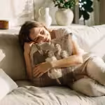 A woman hugging a custom photo pillow in a sunlit living room.