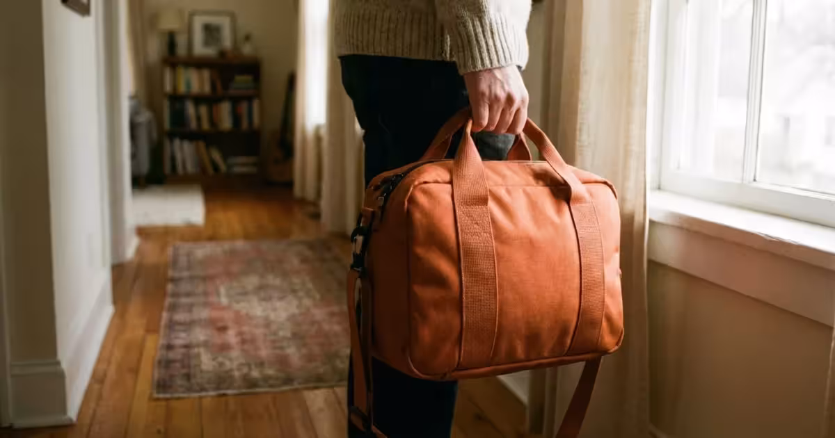 A person holding a waterproof orange emergency bag in a home hallway, symbolizing disaster preparedness.