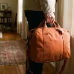 A person holding a waterproof orange emergency bag in a home hallway, symbolizing disaster preparedness.