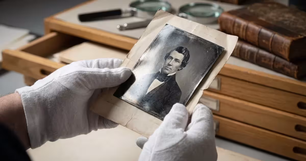 White-gloved hands holding an antique black and white photo with visible silvering sheen.