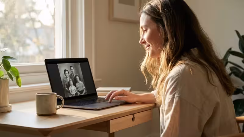 A woman looks at a digital family photo on her laptop in a bright, sunlit home office.