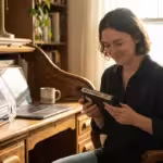 A person at a bright desk holding a VHS tape next to a laptop, representing the bridge between analog and digital.